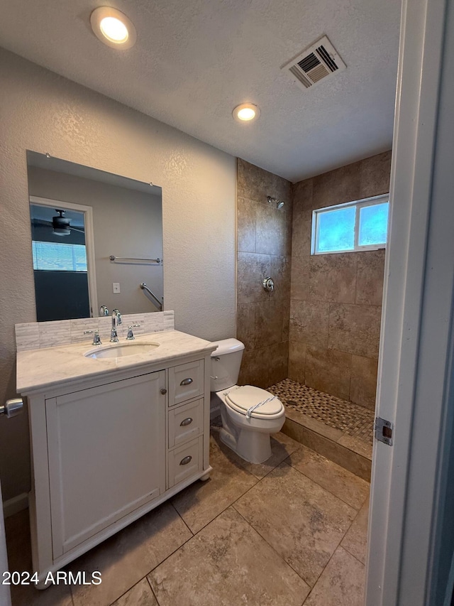 bathroom with a tile shower, vanity, a textured ceiling, and toilet