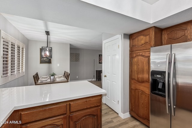 kitchen featuring stainless steel fridge, decorative light fixtures, and light wood-type flooring