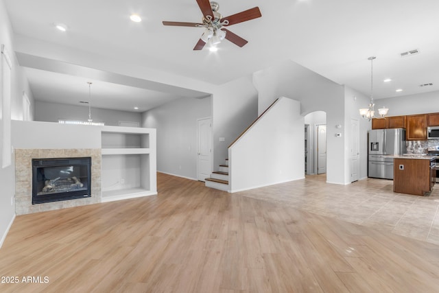 unfurnished living room featuring ceiling fan with notable chandelier, light hardwood / wood-style floors, a tile fireplace, and built in features