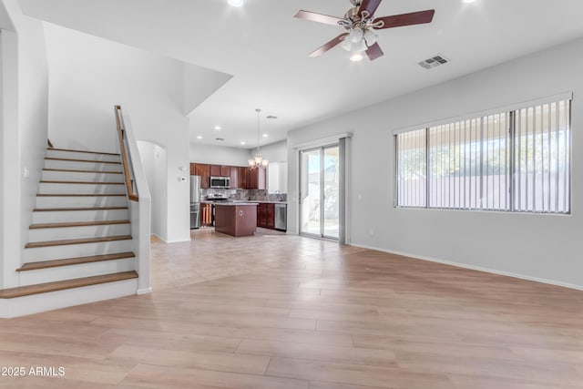 unfurnished living room with ceiling fan with notable chandelier and light hardwood / wood-style flooring