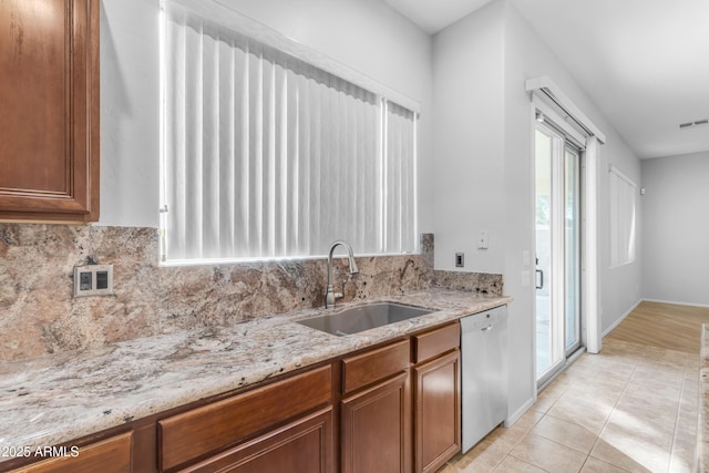 kitchen with decorative backsplash, sink, light stone counters, light tile patterned floors, and stainless steel dishwasher