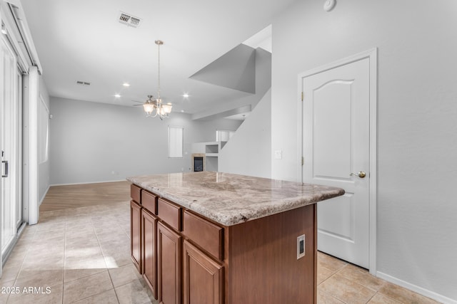 kitchen with a kitchen island, decorative light fixtures, a notable chandelier, light stone counters, and light tile patterned floors