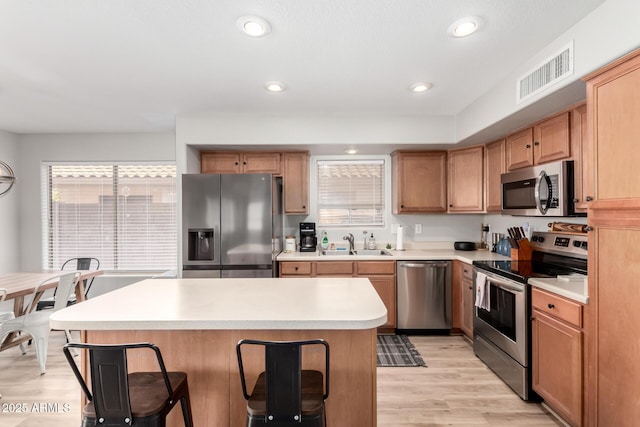 kitchen with sink, stainless steel appliances, a center island, a kitchen bar, and light wood-type flooring