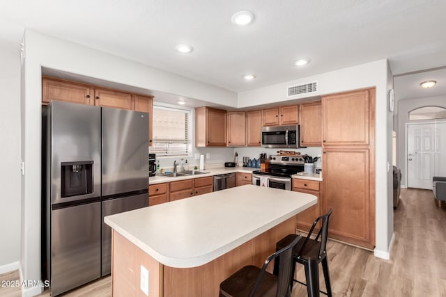 kitchen featuring a kitchen island, appliances with stainless steel finishes, sink, a kitchen bar, and light hardwood / wood-style flooring