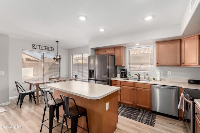 kitchen with a kitchen island, appliances with stainless steel finishes, sink, hanging light fixtures, and light hardwood / wood-style flooring