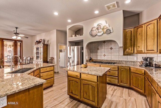 kitchen with a sink, stainless steel fridge with ice dispenser, a center island with sink, gas stovetop, and visible vents