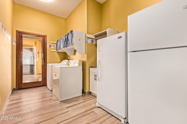 clothes washing area featuring baseboards, cabinet space, washing machine and dryer, and light wood-style floors