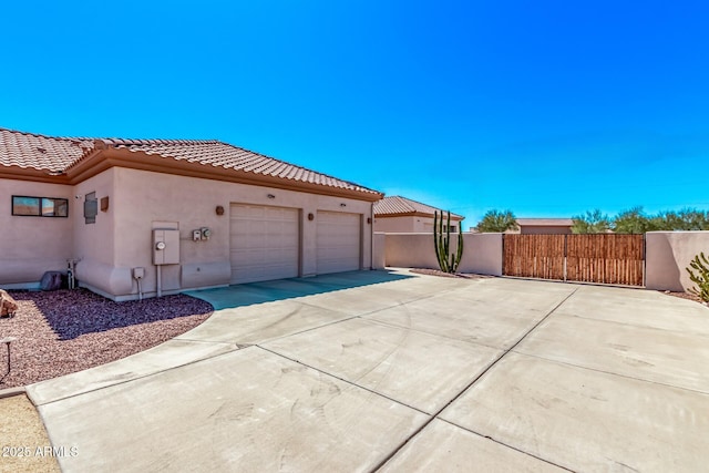 view of side of home featuring a tile roof, stucco siding, an attached garage, and driveway