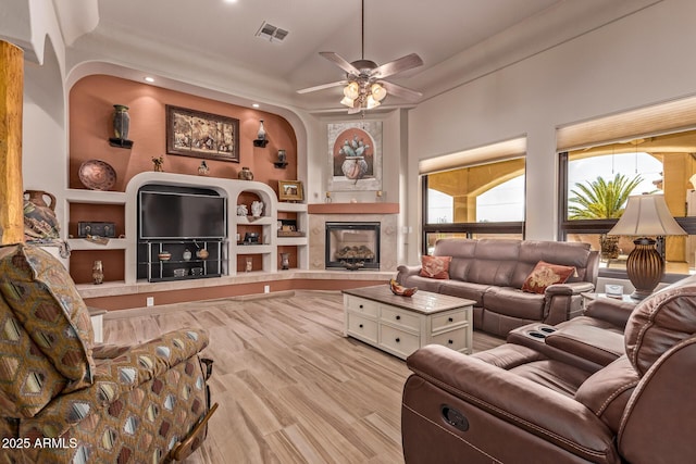 living area featuring vaulted ceiling, visible vents, a ceiling fan, a fireplace, and wood finished floors