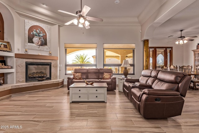 living area with arched walkways, a tile fireplace, wood finish floors, and a ceiling fan