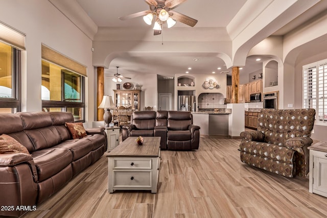 living area featuring arched walkways, a ceiling fan, and light wood finished floors