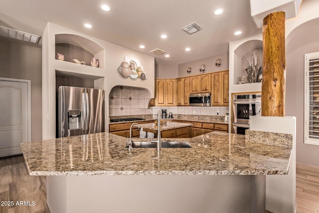 kitchen featuring light stone countertops, a sink, tasteful backsplash, and appliances with stainless steel finishes