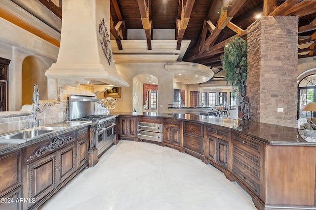 kitchen with sink, custom exhaust hood, range with two ovens, tasteful backsplash, and kitchen peninsula