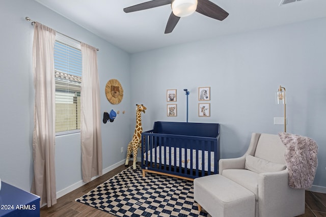 bedroom with ceiling fan, a nursery area, and dark hardwood / wood-style floors