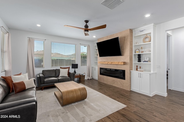 living room with ceiling fan, built in features, dark hardwood / wood-style floors, and a large fireplace