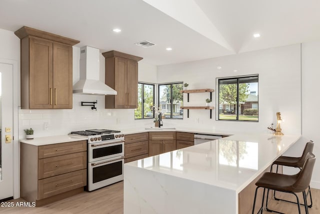 1338 E Granada Rd, Phoenix, AZ 85006 - kitchen featuring range with two ovens, wall chimney exhaust hood, a peninsula, a kitchen bar, and backsplash