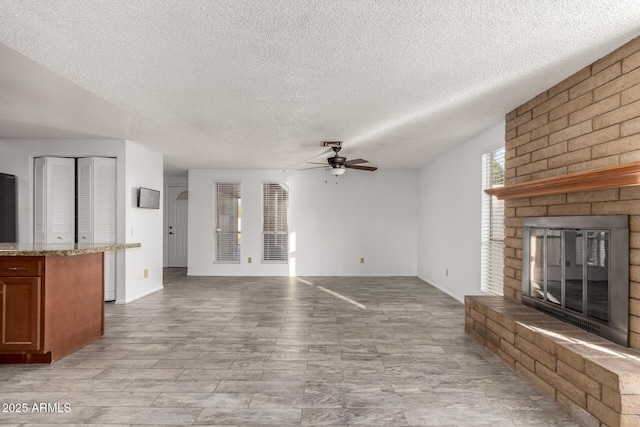 unfurnished living room featuring a brick fireplace, a textured ceiling, and ceiling fan