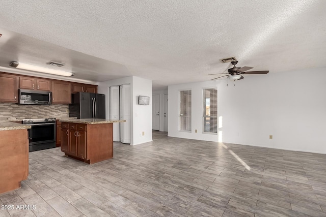 kitchen featuring decorative backsplash, a center island, ceiling fan, stainless steel appliances, and light stone countertops