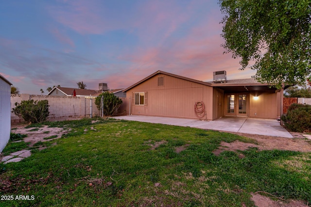 back house at dusk with a patio, central AC, and a lawn