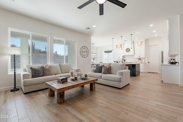 living room featuring ceiling fan, sink, and light wood-type flooring