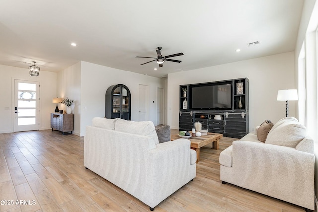 living room featuring ceiling fan with notable chandelier and light hardwood / wood-style floors