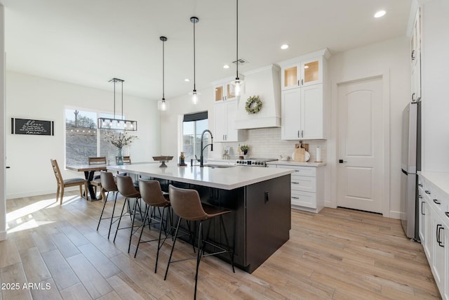 kitchen with sink, custom range hood, white cabinets, a center island with sink, and decorative backsplash