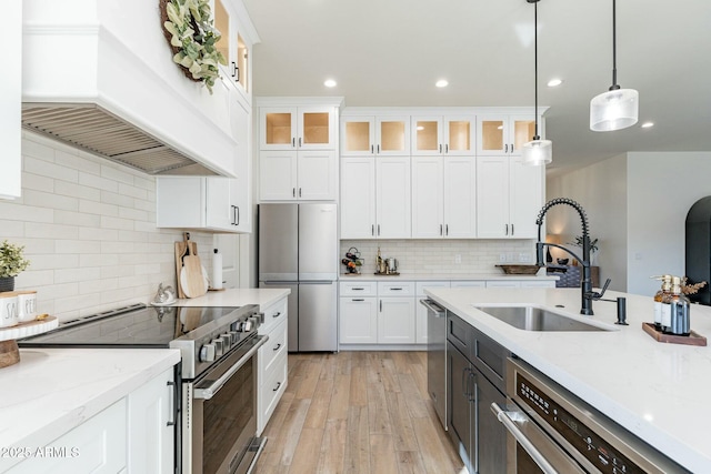 kitchen featuring appliances with stainless steel finishes, white cabinetry, sink, hanging light fixtures, and custom range hood