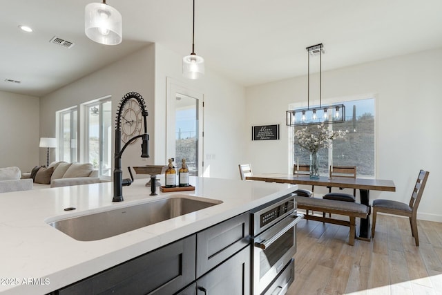 kitchen with pendant lighting, sink, light stone counters, and light wood-type flooring