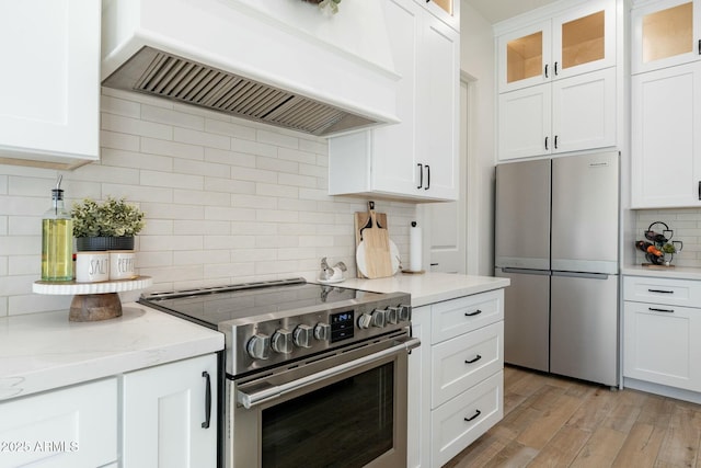 kitchen with white cabinetry, appliances with stainless steel finishes, light stone counters, and custom range hood