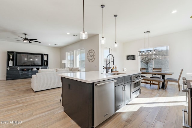 kitchen featuring sink, stainless steel appliances, a center island with sink, decorative light fixtures, and light wood-type flooring