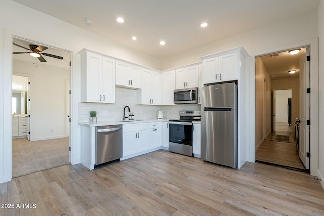 kitchen featuring sink, stainless steel appliances, tasteful backsplash, light hardwood / wood-style floors, and white cabinets