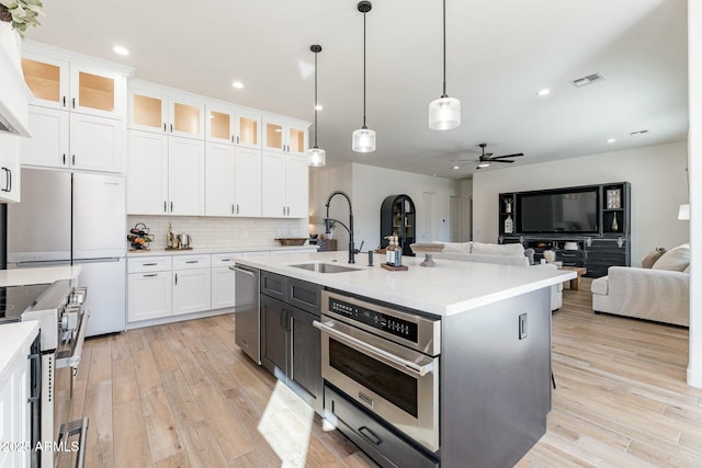 kitchen with sink, white cabinetry, hanging light fixtures, appliances with stainless steel finishes, and an island with sink