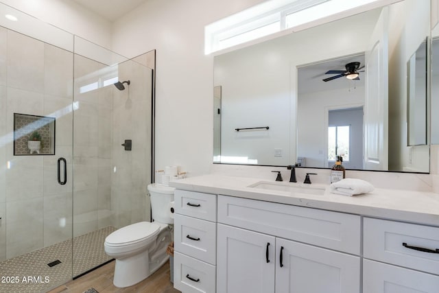 bathroom featuring hardwood / wood-style floors, a shower with shower door, vanity, ceiling fan, and toilet