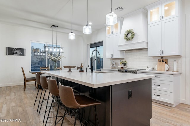 kitchen with a kitchen island with sink, pendant lighting, custom exhaust hood, and white cabinets