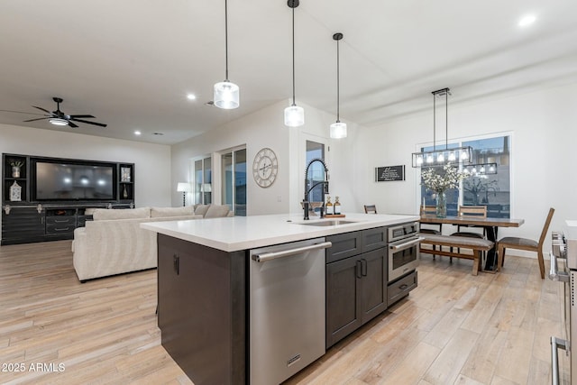 kitchen with appliances with stainless steel finishes, pendant lighting, an island with sink, sink, and light hardwood / wood-style flooring