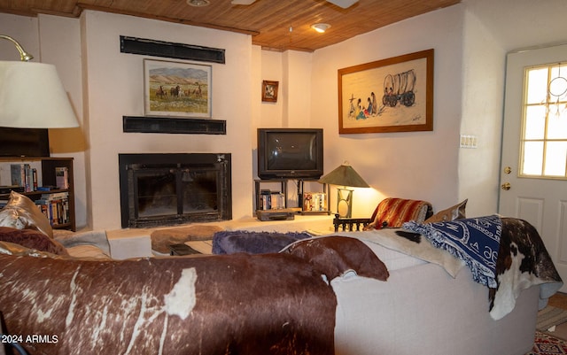 living area featuring wood ceiling and a glass covered fireplace
