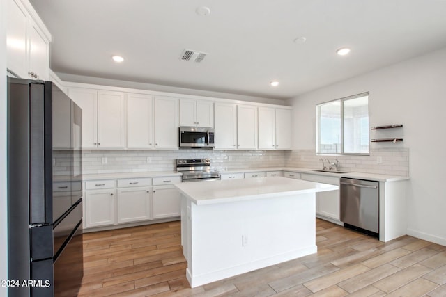 kitchen featuring tasteful backsplash, stainless steel appliances, white cabinets, light wood-type flooring, and a kitchen island