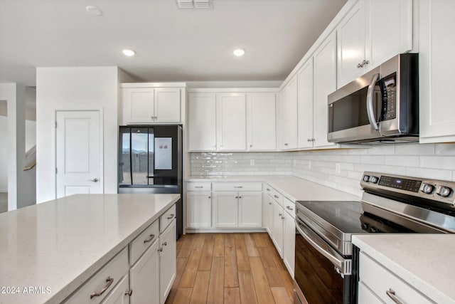 kitchen featuring white cabinetry, stainless steel appliances, decorative backsplash, light stone counters, and light hardwood / wood-style floors