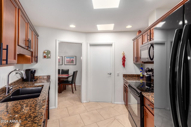 kitchen with sink, a skylight, dark stone countertops, and black appliances