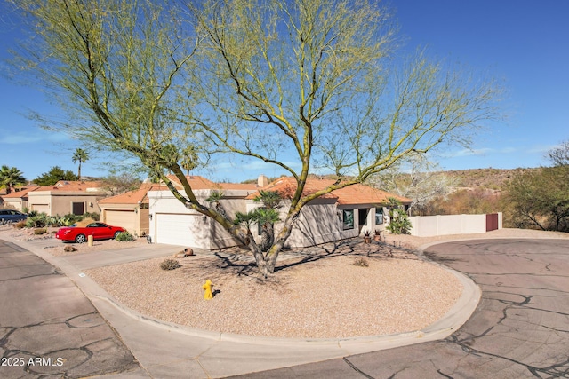 view of front of house with a tile roof, stucco siding, concrete driveway, fence, and a garage