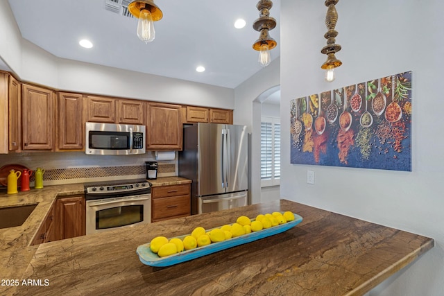 kitchen with a peninsula, appliances with stainless steel finishes, brown cabinets, and hanging light fixtures