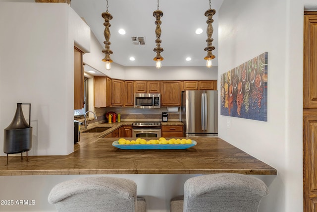 kitchen with a peninsula, a sink, visible vents, a kitchen breakfast bar, and appliances with stainless steel finishes