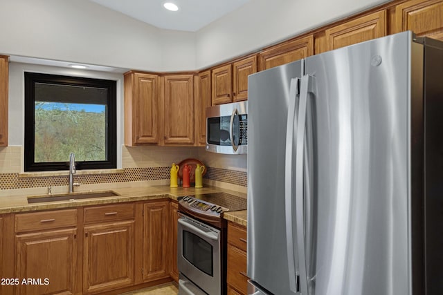 kitchen with light stone counters, stainless steel appliances, a sink, tasteful backsplash, and brown cabinetry