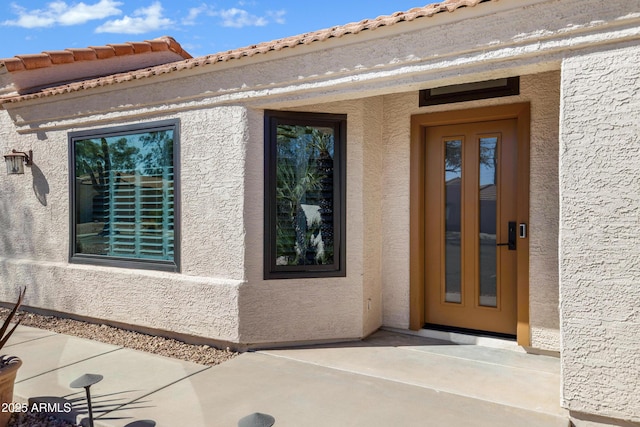 view of exterior entry with a patio, a tile roof, and stucco siding