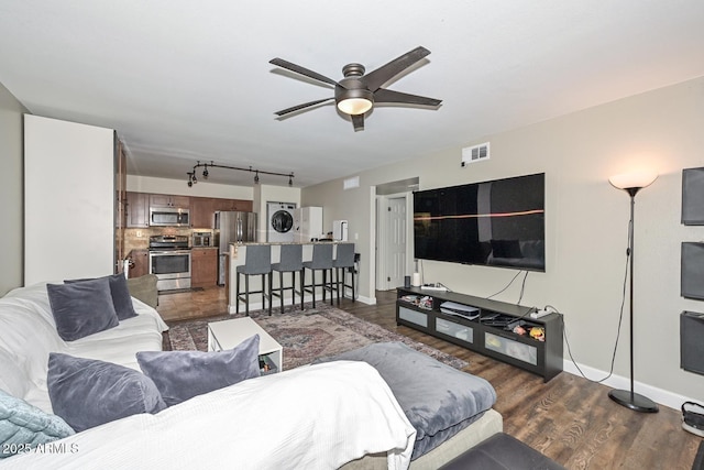 living room featuring ceiling fan, stacked washer and dryer, dark wood-type flooring, and track lighting