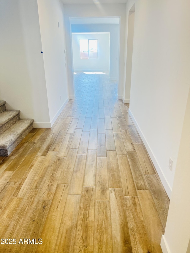 hall with light wood-style flooring, stairs, and baseboards