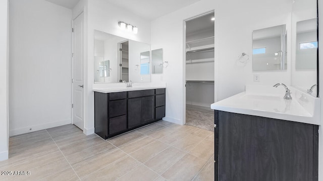 full bath with two vanities, a walk in closet, baseboards, and tile patterned floors