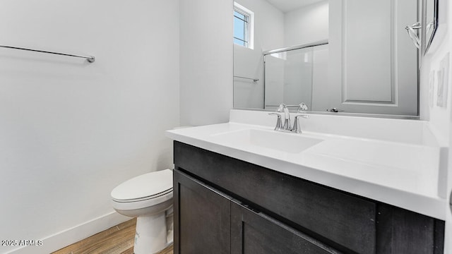 bathroom featuring toilet, wood finished floors, vanity, baseboards, and a shower with door