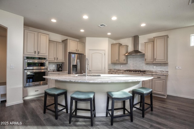 kitchen featuring sink, appliances with stainless steel finishes, an island with sink, a kitchen bar, and wall chimney exhaust hood