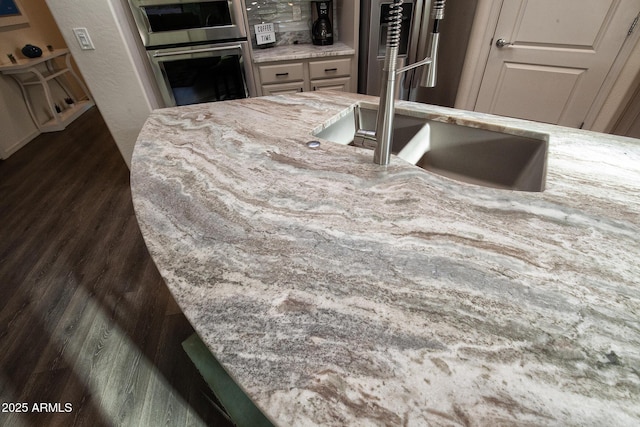 kitchen with light stone counters, sink, stainless steel double oven, and refrigerator